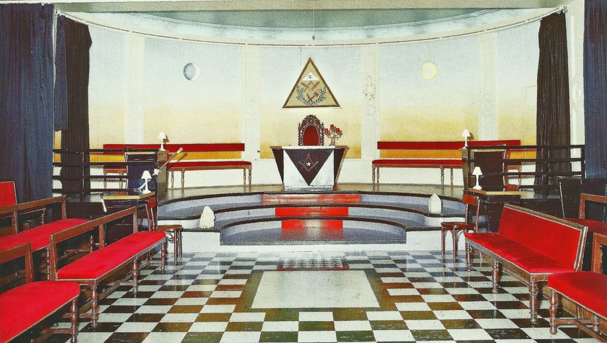 Intérieur d'un temple : sièges rouges, dallage en damier noir et blanc, autel et delta lumineux